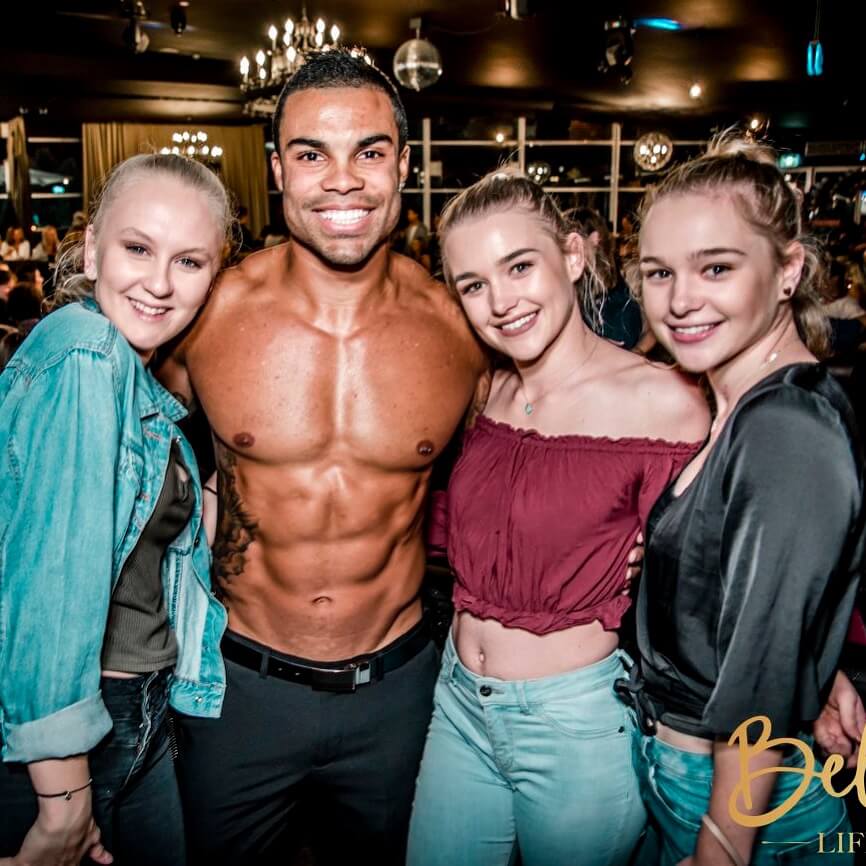 tanned and ripped topless waiter with arms around girls