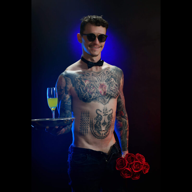 topless waiter with tattoos serving a tray of champagne