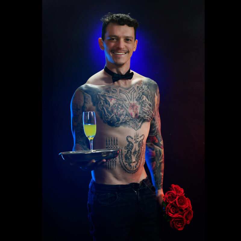 tattooed topless waiter holding tray of champagne and flowers